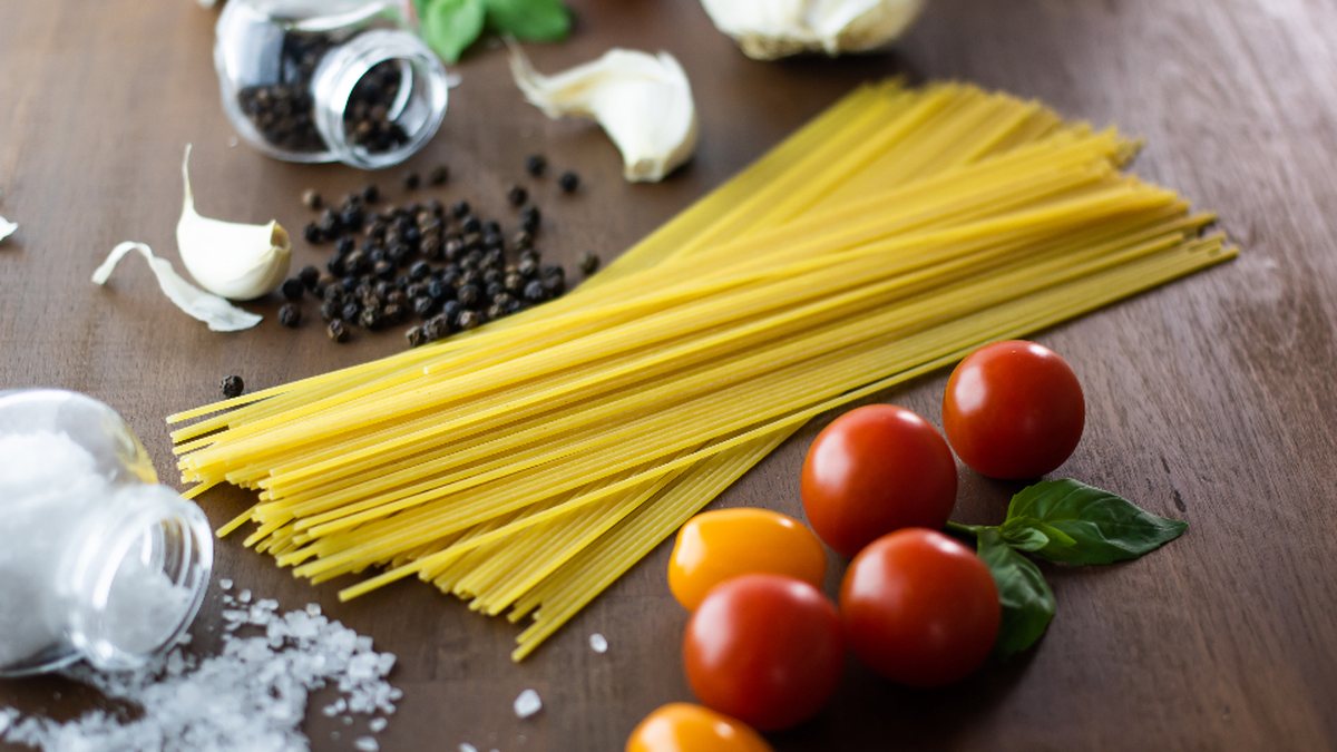 Spaghetti, cherry tomatoes, garlic, basil and peppercorns on a wooden table